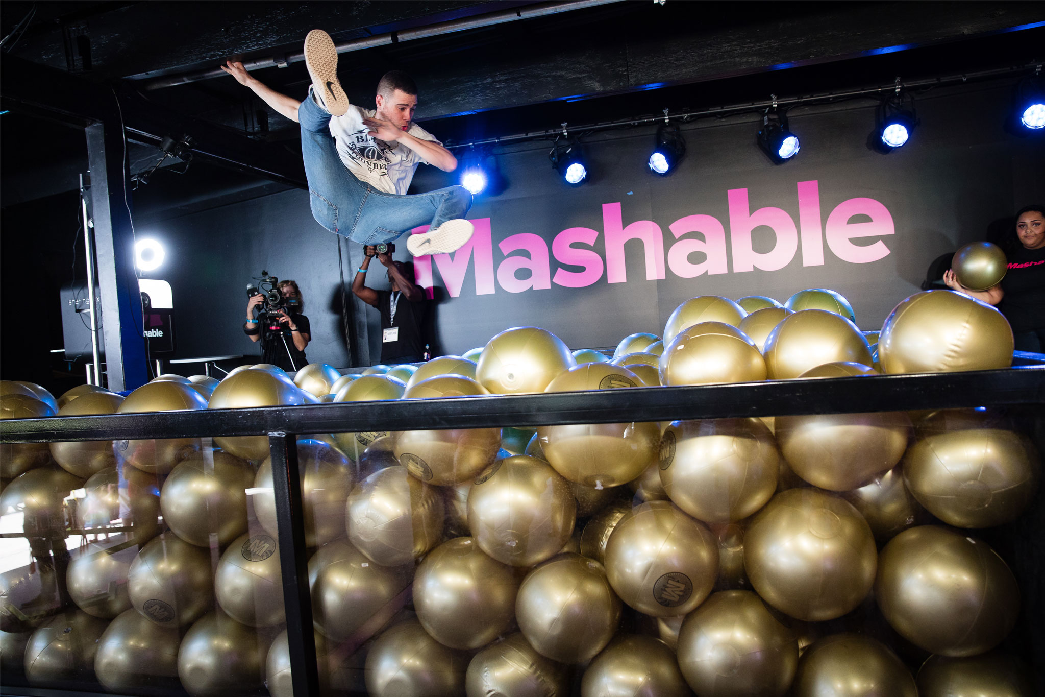 Picture of event goer jumping in custom made ball pit with Mashable sign in background.