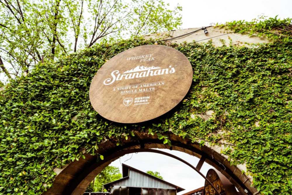Picture of a Stranahans Whiskey sign hung amidst an archway of ivy at the entrance to the event.