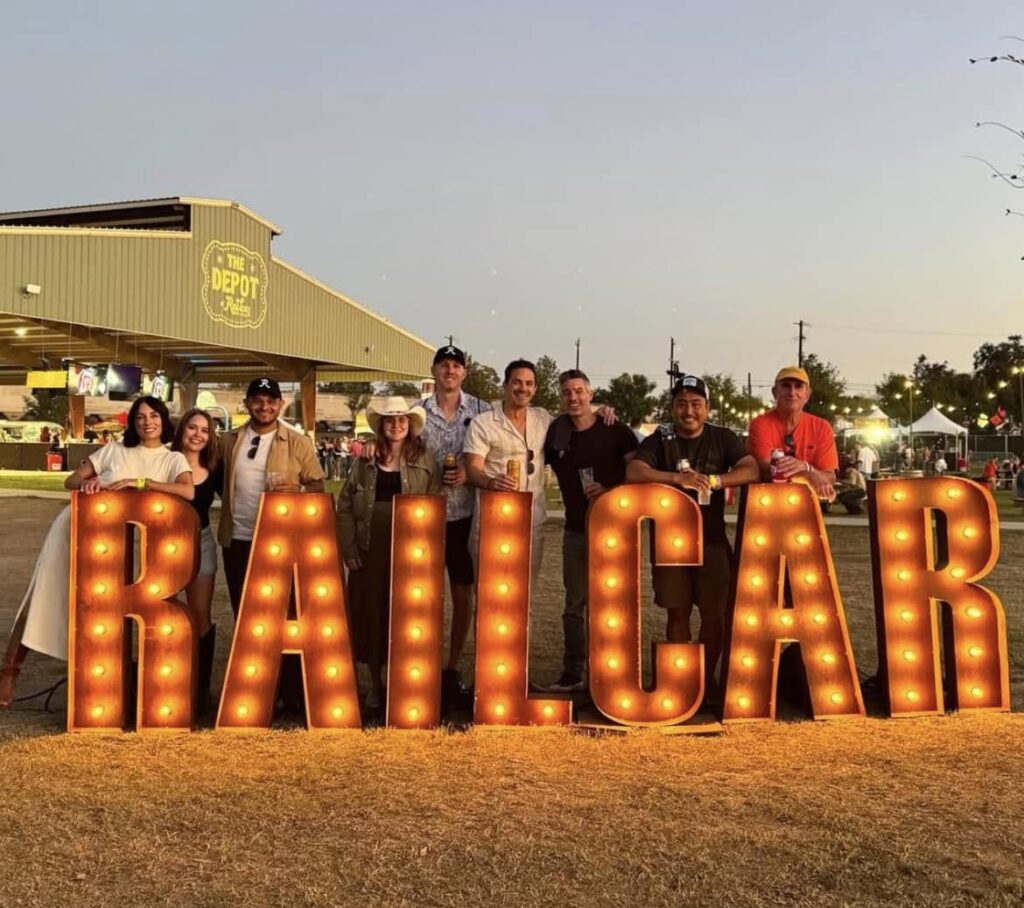 Marquee letters with bulbs inside spelling RAILCAR as festival attendees pose behind the letters as a photoop.